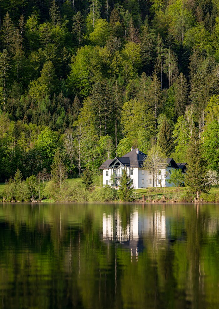 Serene lakeside house surrounded by lush forest in Ebensee, reflecting on calm waters.