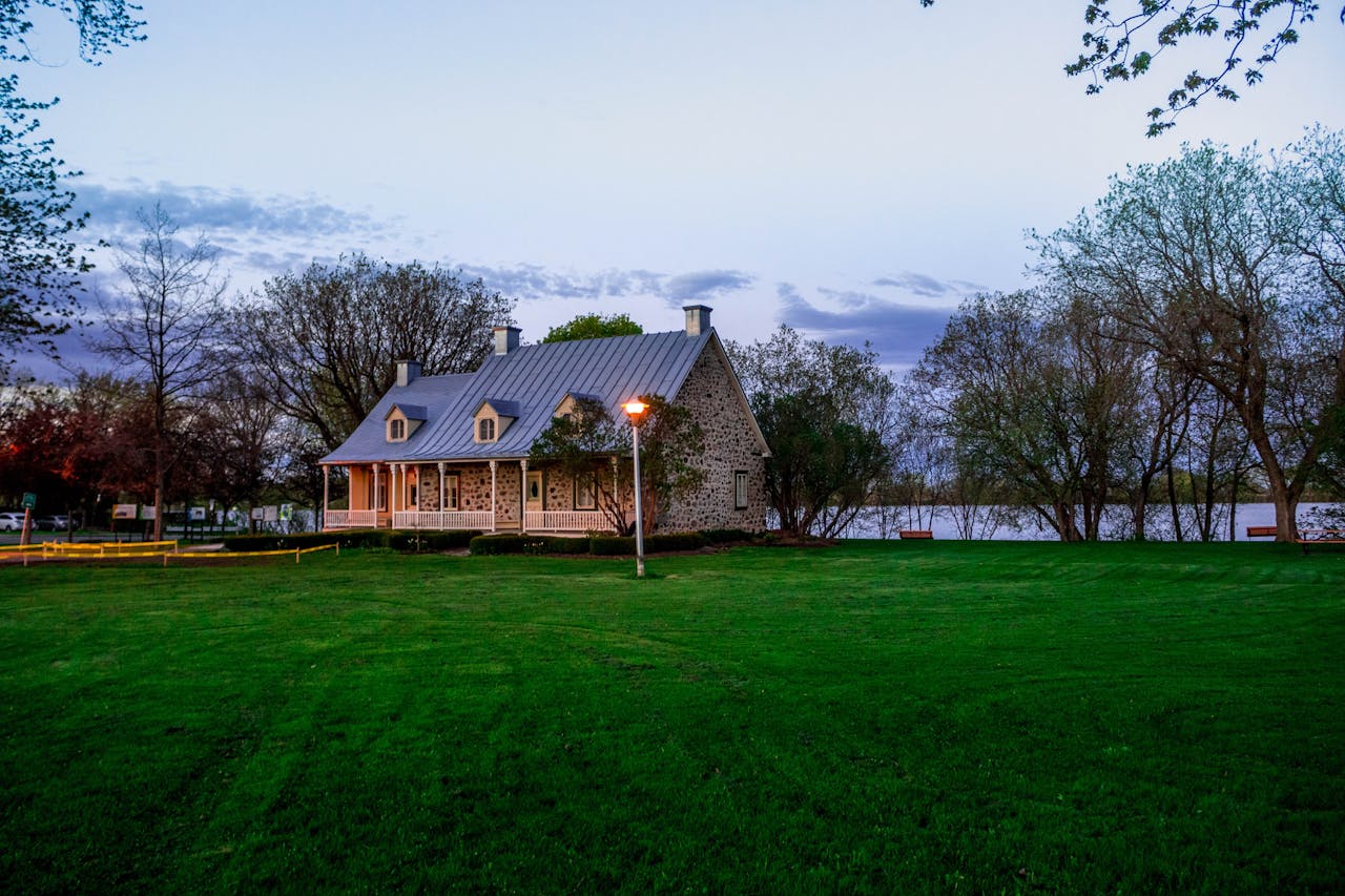 Serene stone house by a lakeside with lush green lawn, ideal for real estate and architectural themes.
